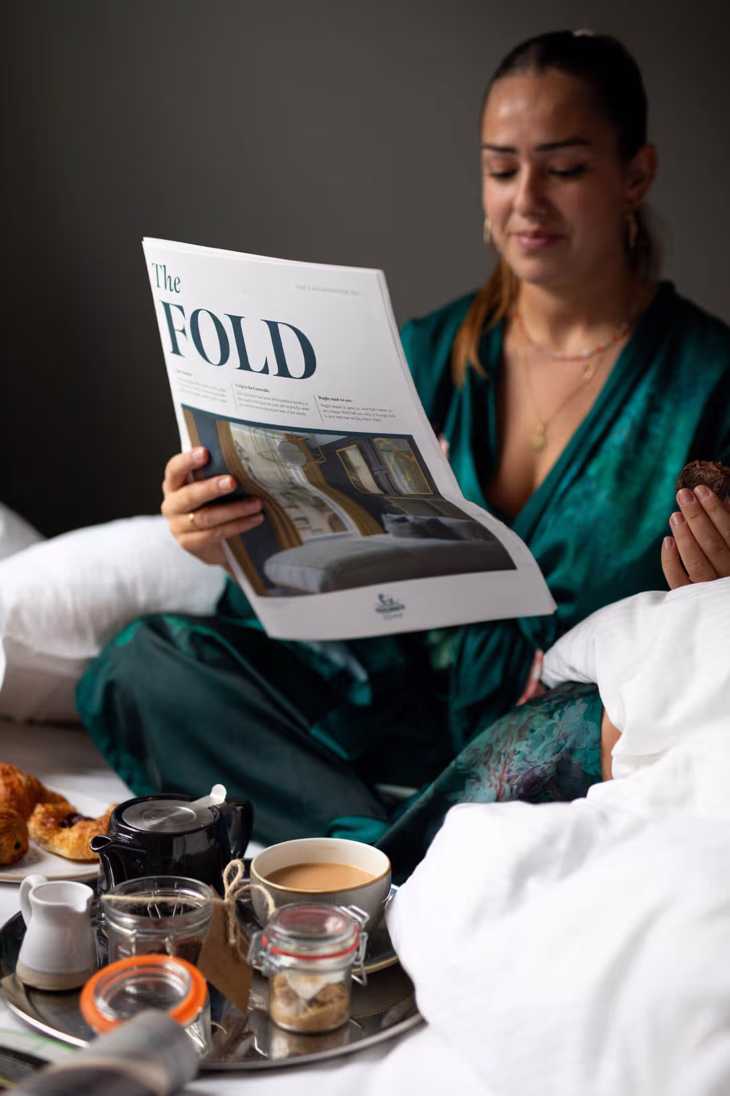 woman reading an issue of Young's in-house newspaper, The Fold, in bed with a tray of coffee and pastries in front of her