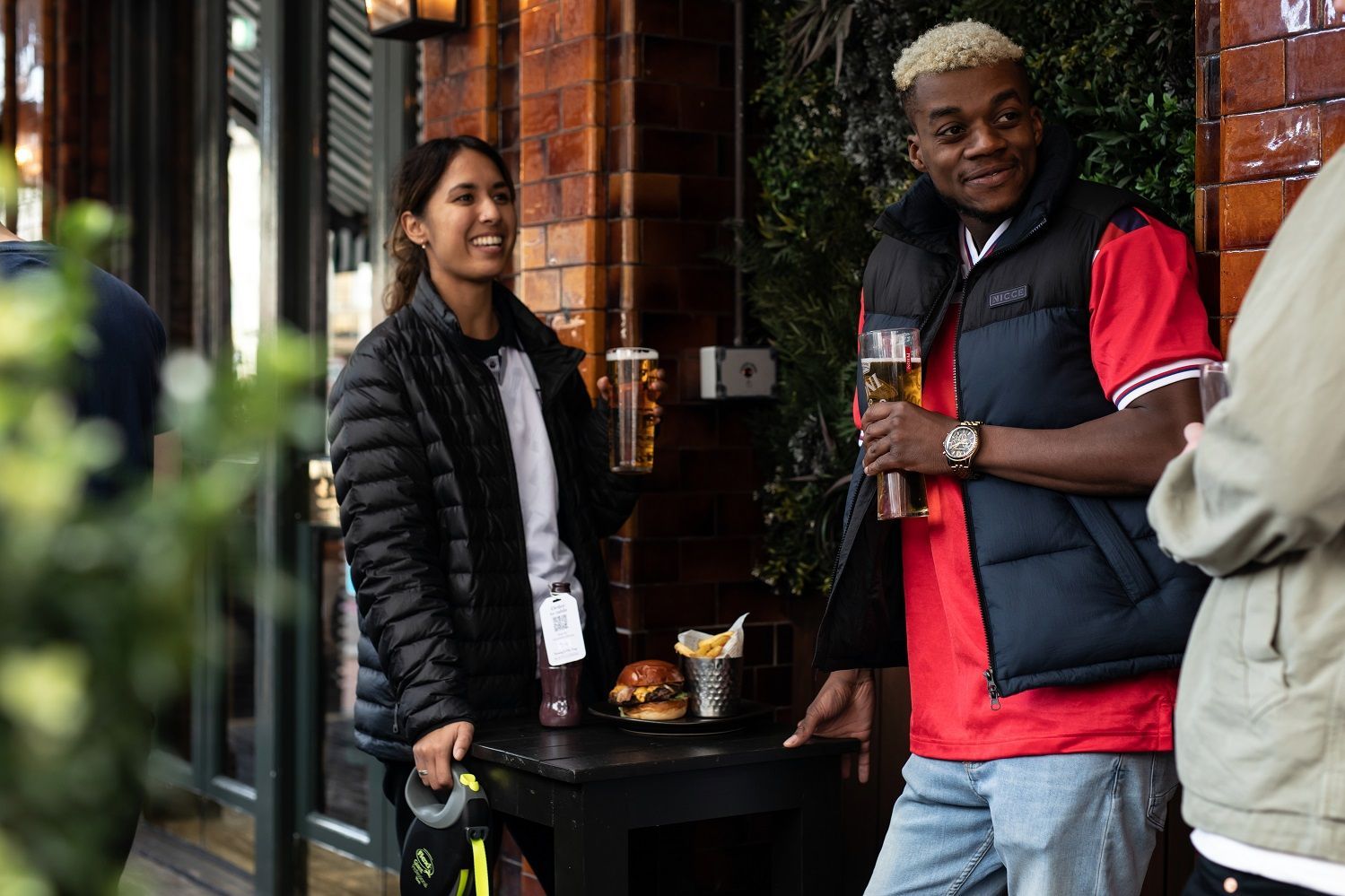 friends standing around a table with a tray of food while drinking Young's pints