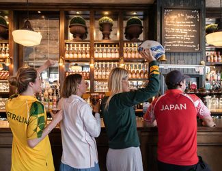 friends wearing rugby jerseys while standing in front of a bar holding a rugby ball and Young's pints